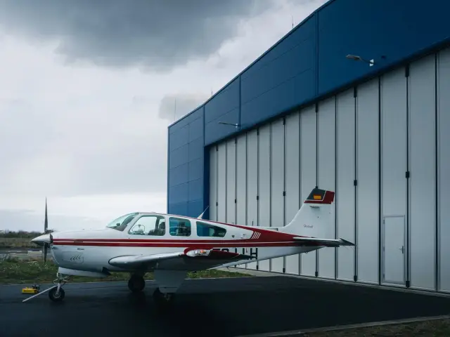 Red and white Beechcraft Bonanza in front of the hangar