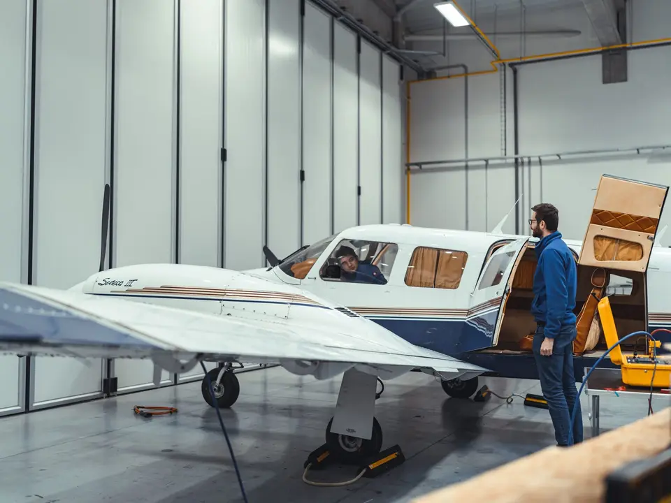 Technician with a yellow test case beside a light aircraft with the door open in the hangar