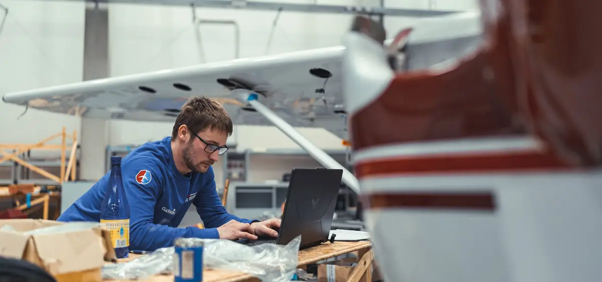 Avionics technician with a laptop at a bench beside a light aircraft in the hangar